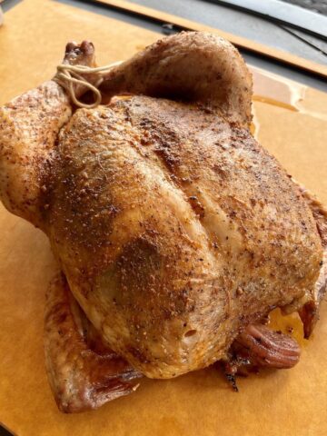 whole browned chicken on a large wood cutting board