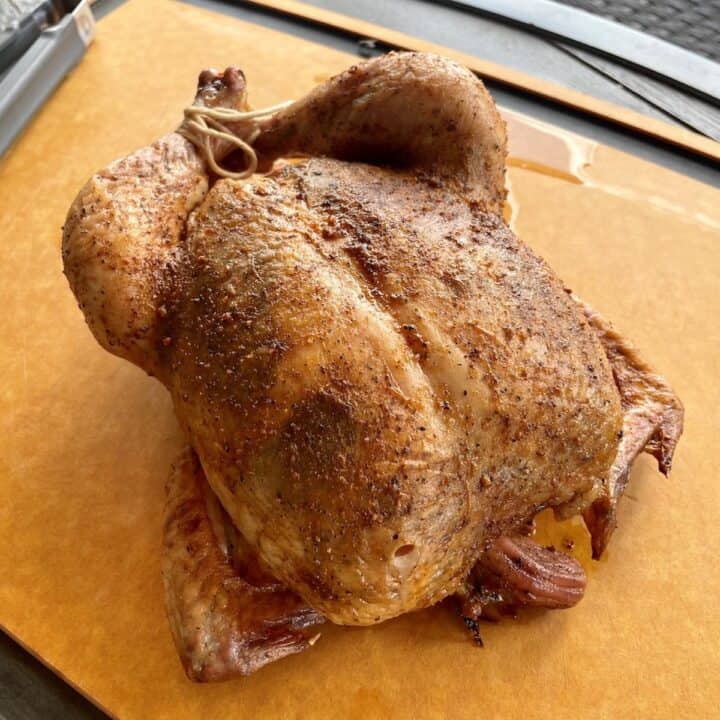 whole browned chicken on a large wood cutting board