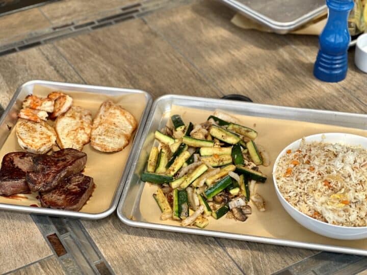 silver trays with cooked hibachi steak chicken vegetables and fried rice in a white bowl