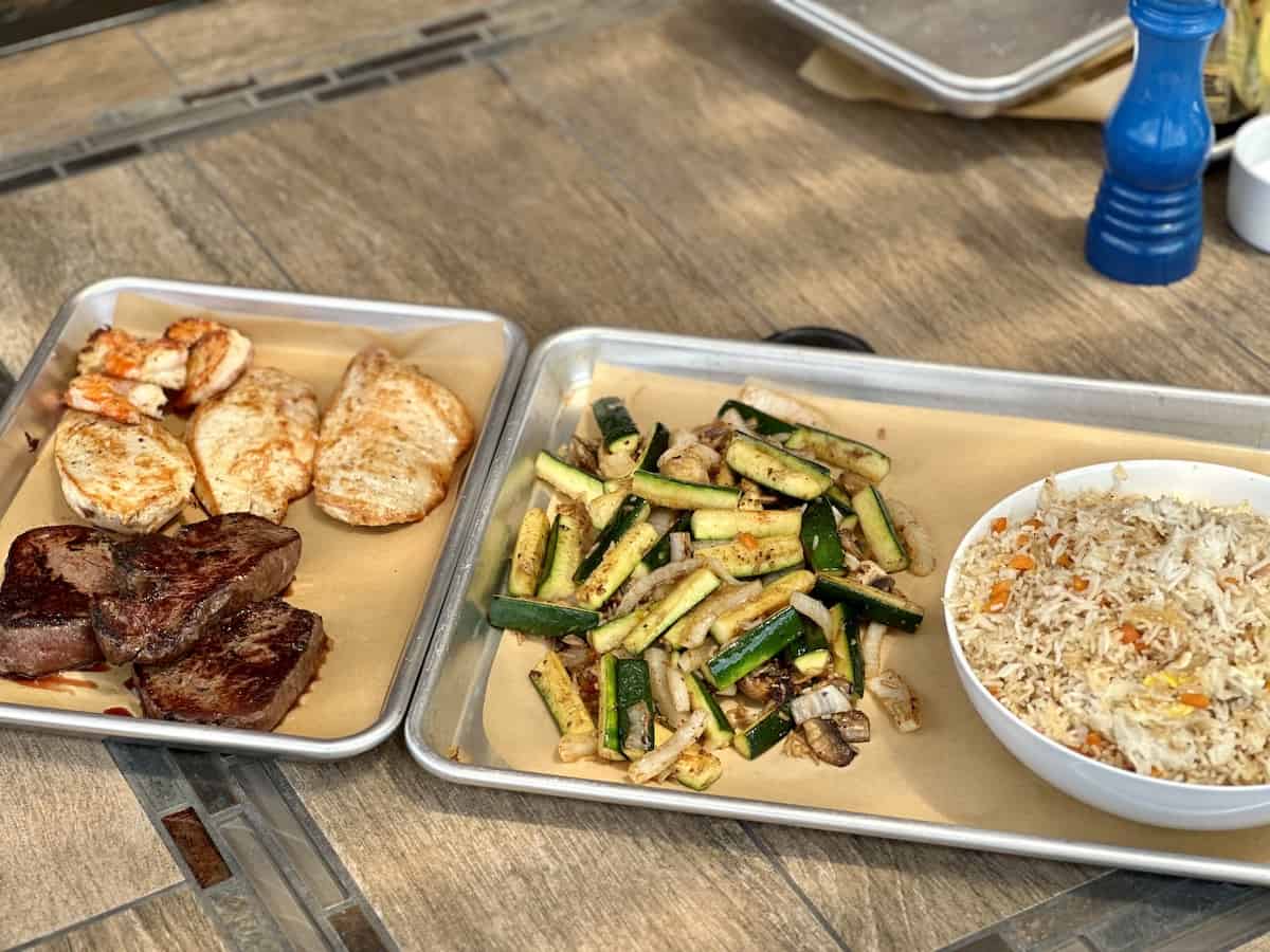 silver trays with cooked hibachi steak chicken vegetables and fried rice in a white bowl
