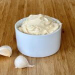 white bowl of prepared hibachi garlic butter on a wood cutting board with two cloves of garlic