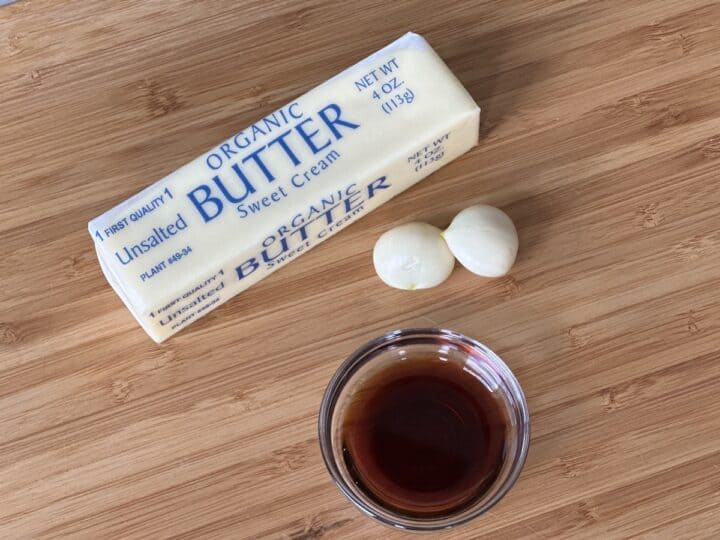 one stick butter 2 garlic cloves small glass bowl soy sauce on a wood cutting board
