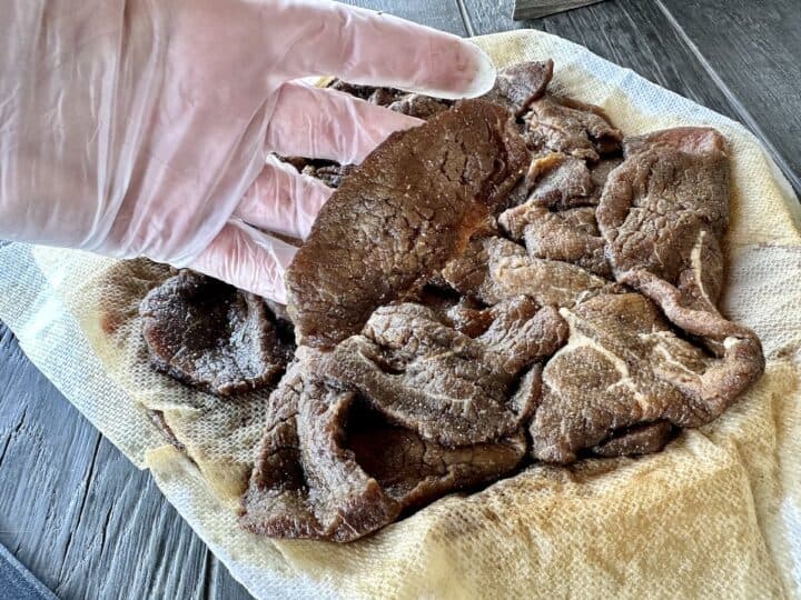 gloved hand holding marinating sliced beef and white plate of marinated sliced beef 