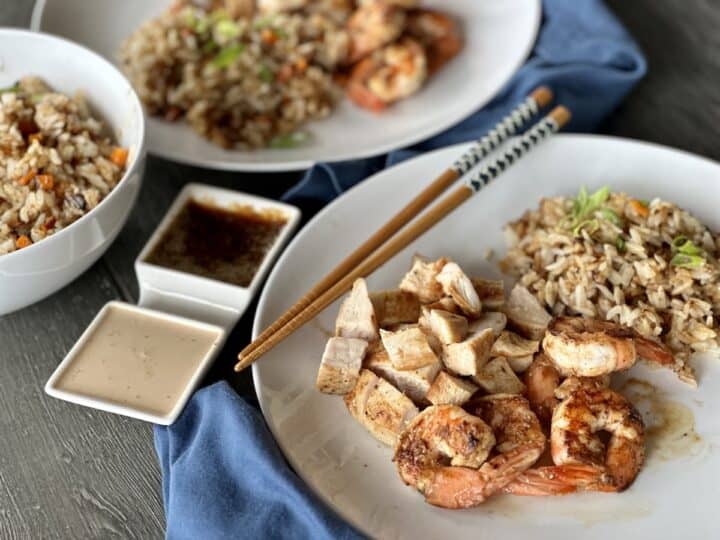 white dishes of hibachi chicken and shrimp with fried rice dipping sauces and chopsticks