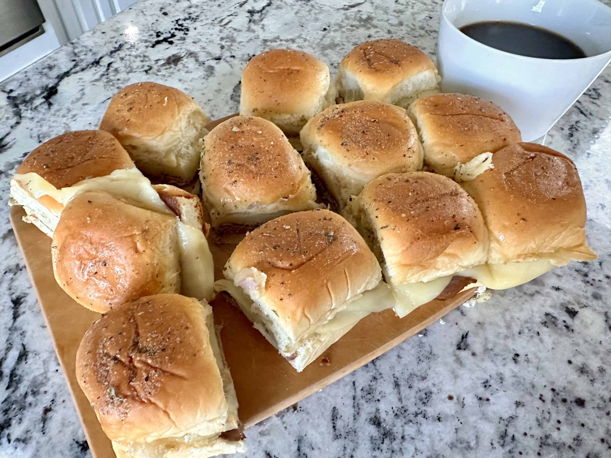 12 beef dip sliders on cutting board white cup of au jus