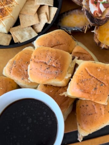 beef dip sliders on cutting board white cup of au jus