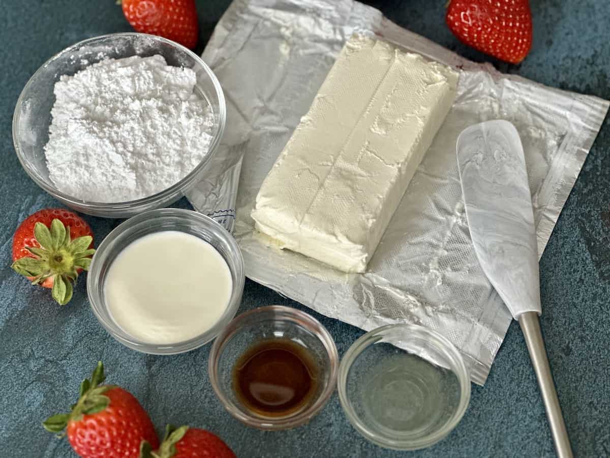 block of cream cheese bowl of powdered sugar vanilla heavy cream lemon juice whole strawberries blue background 