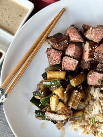 hibachi steak vegetables and fried rice on white place chopsticks and dipping sauce