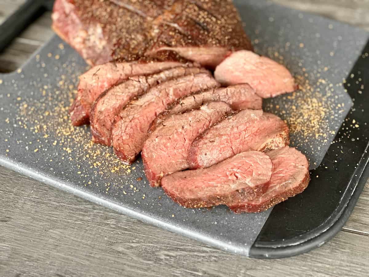 sliced smoked Tri Tip on black cutting and wood plank table