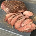 sliced smoked Tri Tip on black cutting board spices and wood table