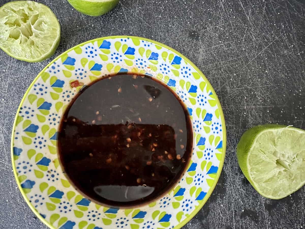 blue and green bowl of beef jerky marinade on black cutting board and limes cut in half