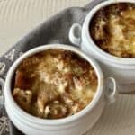 2 white crocks of french onion soup on white table with grey linens