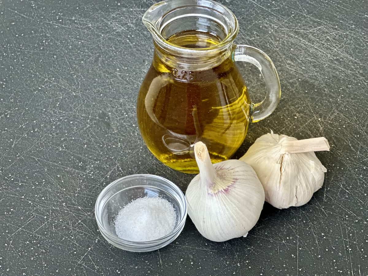 olive oil in glass jar 2 heads of garlic small bowl of salt