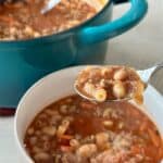 teal pot of soup next to white bowl of pasta e Fagioli with soup spoon