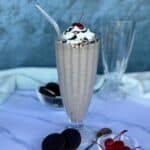 cookies and cream milkshake in tall glass with straw bowl of Oreo cookies bowl of cherries