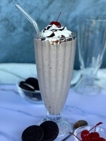 cookies and cream milkshake in tall glass with straw bowl of Oreo cookies bowl of cherries