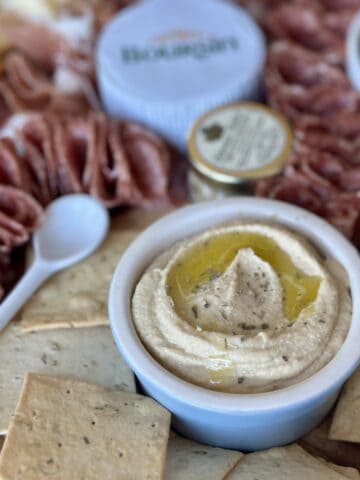 small white spoon folded salami square crackers blue blow of hummus small jarred mustard Boursin cheese