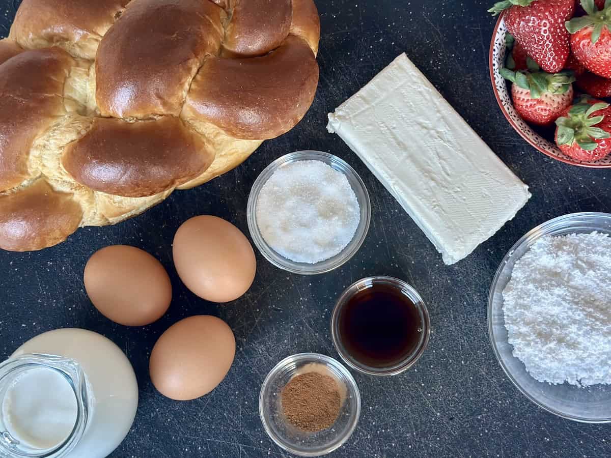 challah bread loaf and other French toast ingredients on black cutting board