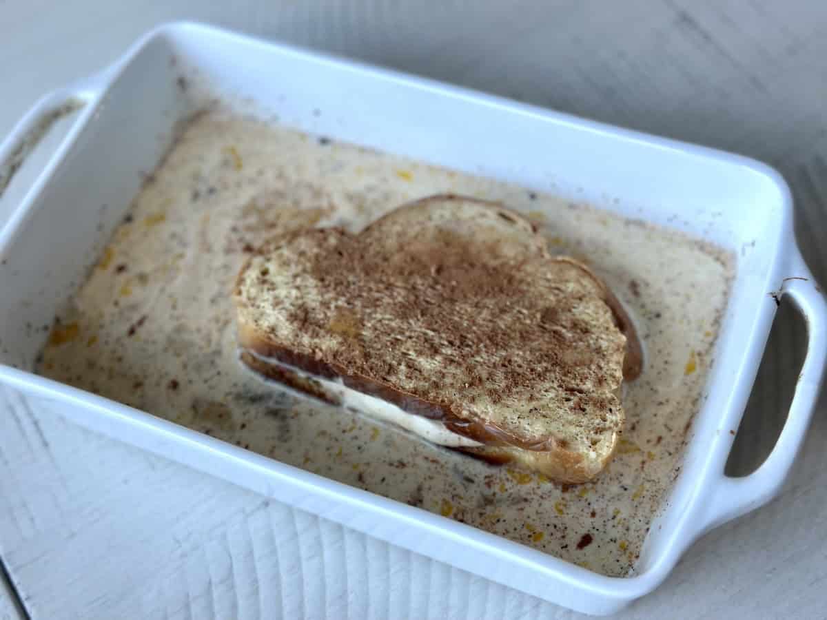 thick sliced challah bread in French toast custard shallow white rectangular dish