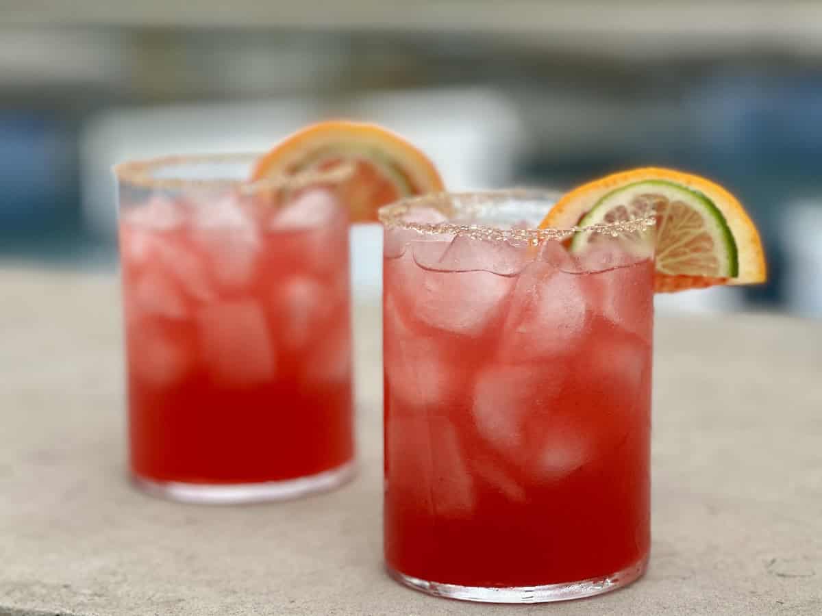 2 prepared blood orange margaritas outside by a pool