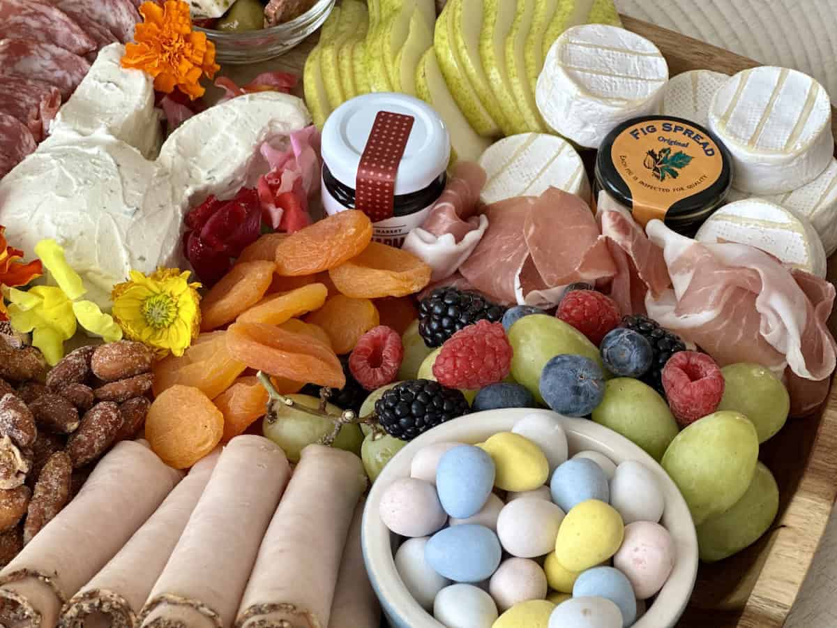 small bowl of chocolate Easter eggs next to other charcuterie board items rolled turkey grapes and berries dried apricots