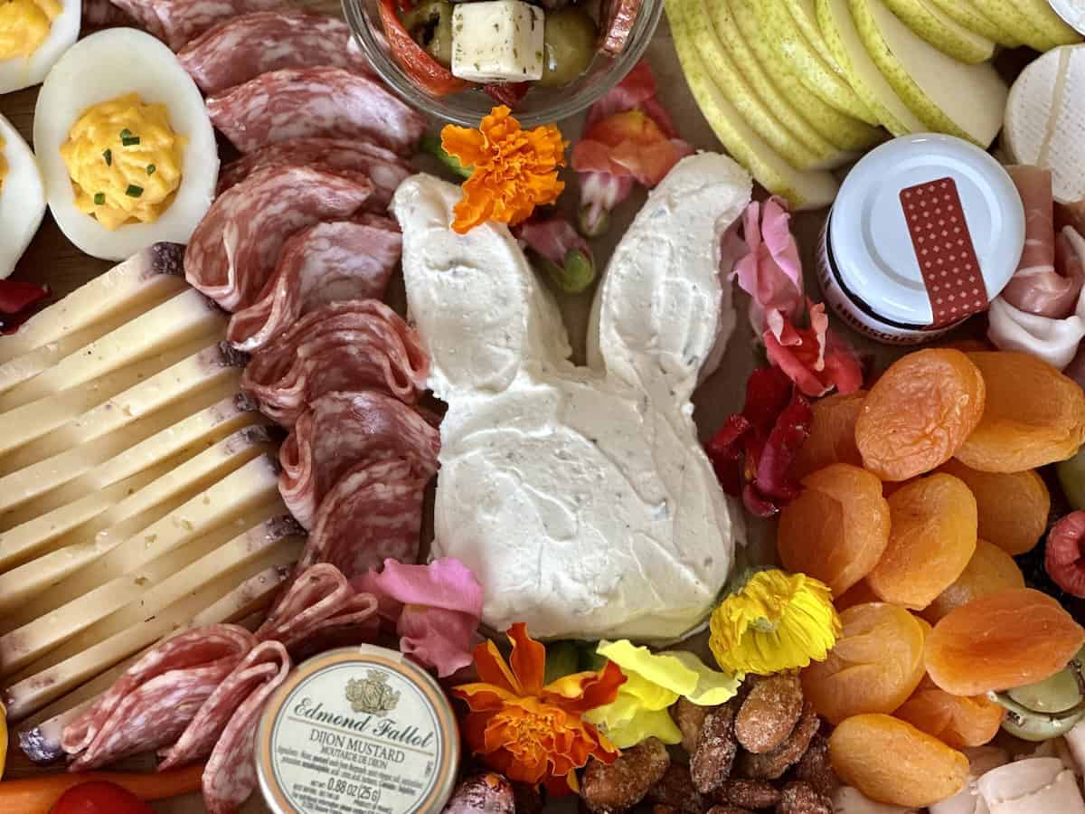 assembled easter charcuterie board with bright colors wrapped chocolate eggs and edible flowers