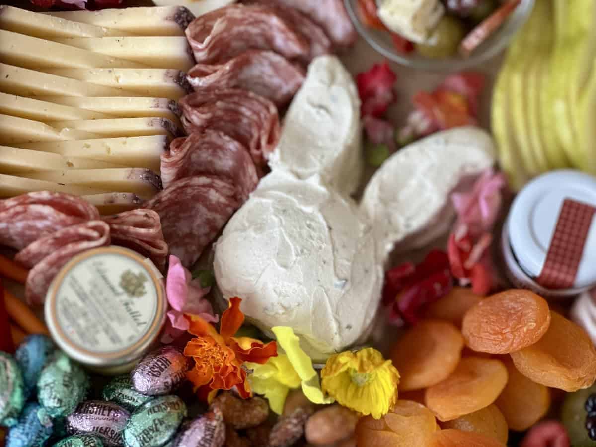 Bunny shaped herb cheese on easter charcuterie board with salami dried fruit sliced cheeses
