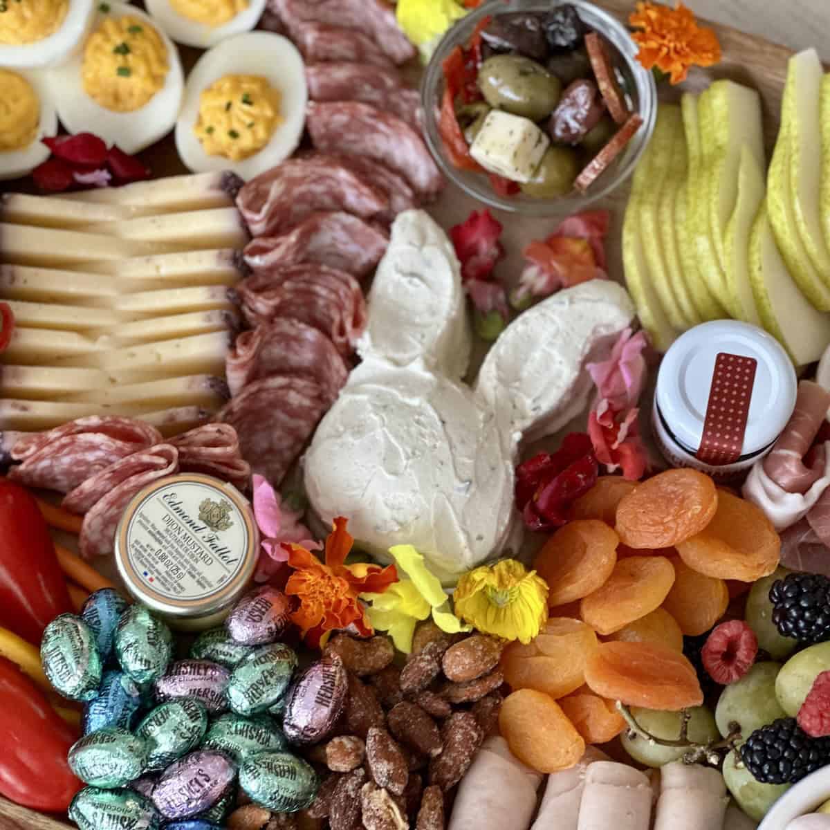 assembled easter charcuterie board with bright colors wrapped chocolate eggs and edible flowers