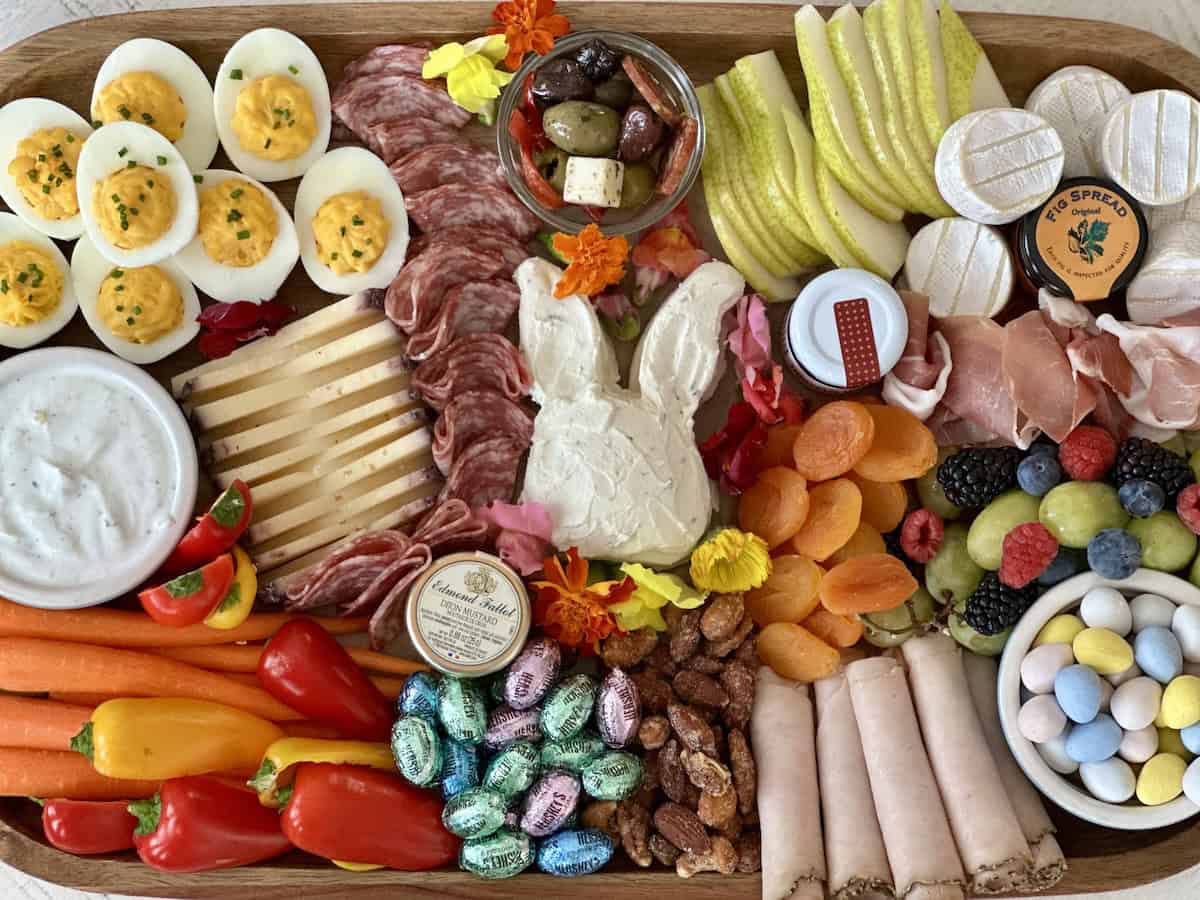 easter charcuterie board with deviled eggs carrots bell pepper and ranch dip a cheese bunny chocolate egg candy cold cuts and assorted snack foods