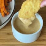 chicken tender dipped in honey mustard sauce in small white bowl