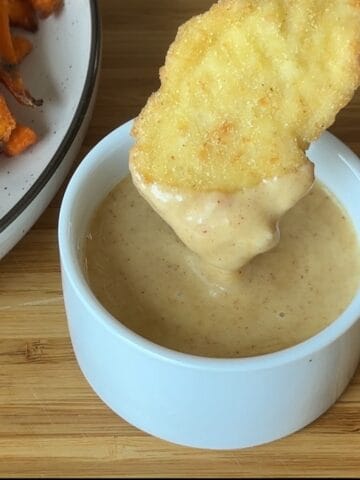 chicken tender dipped in honey mustard sauce in small white bowl