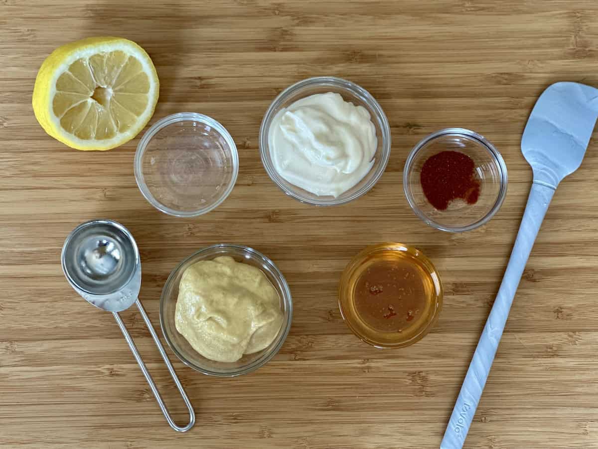small glass bowls with honey mustard sauce ingredients on wood cutting board half a lemon measuring spoon small spatula