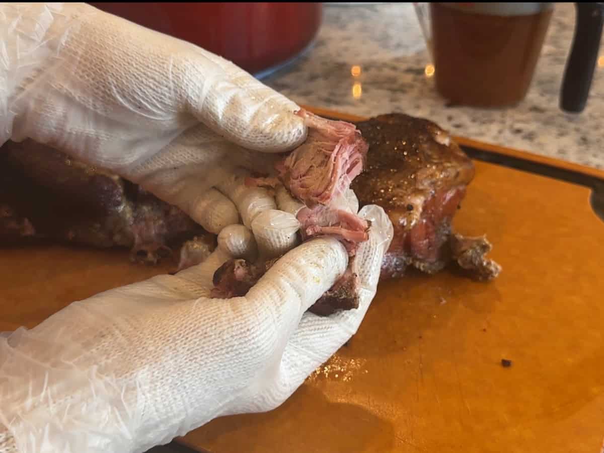 two gloved hands shredding pork meat over wood cutting board