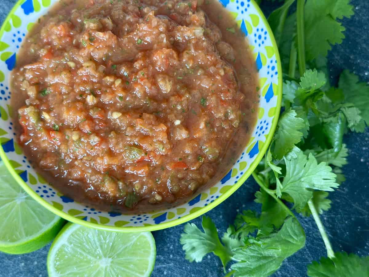 smoked salsa in blue and green bowl with lime cut in half bunch of cilantro black background