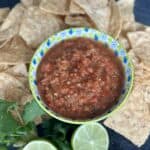 smoked salsa in green and blue bowl tortilla chips lime cut half bunch of cilantro on black cutting board