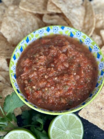 smoked salsa in green and blue bowl tortilla chips lime cut half bunch of cilantro on black cutting board