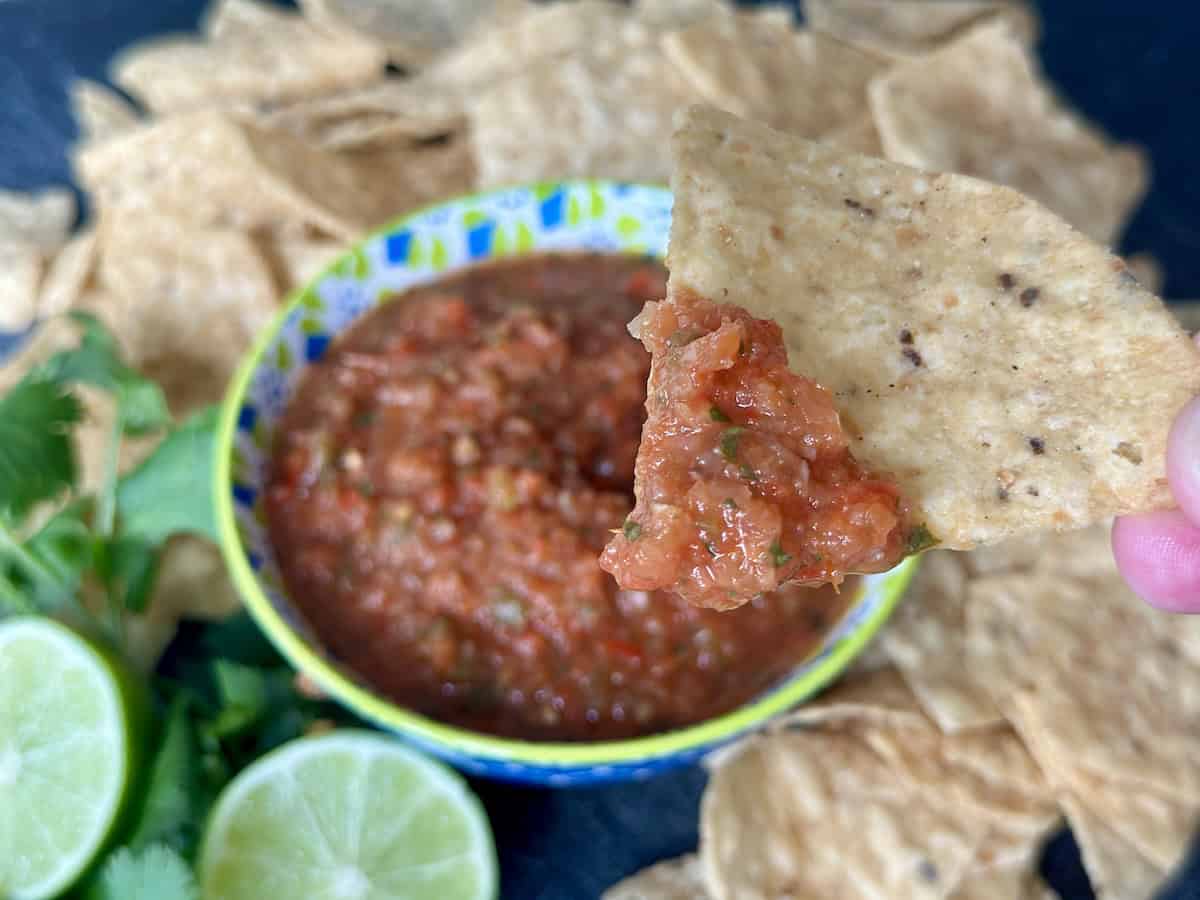 tortilla chip with salsa on it salsa in blue and green bowl surrounded by tortilla chips lime and cilantro
