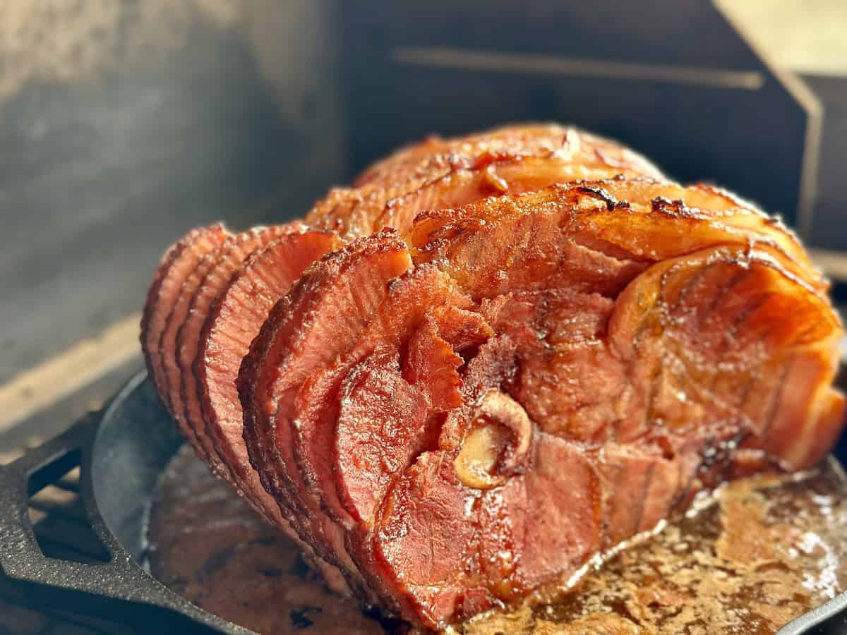 traeger smoked spiral ham in cast iron pan with juices set on a traeger grill