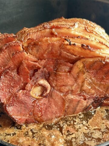 traeger smoked spiral ham in cast iron pan with juices set on a traeger grill