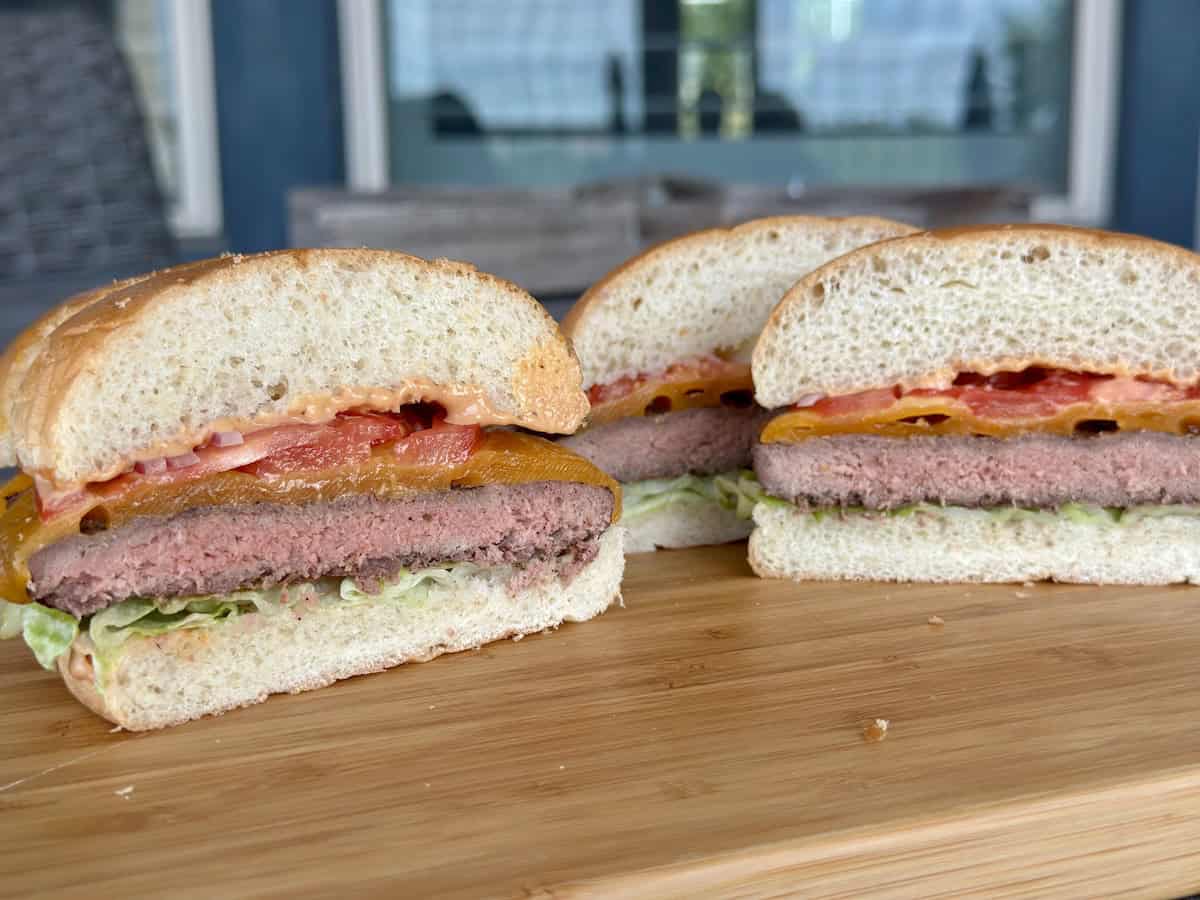 a smoked and grilled cheeseburger cut in half on cutting board