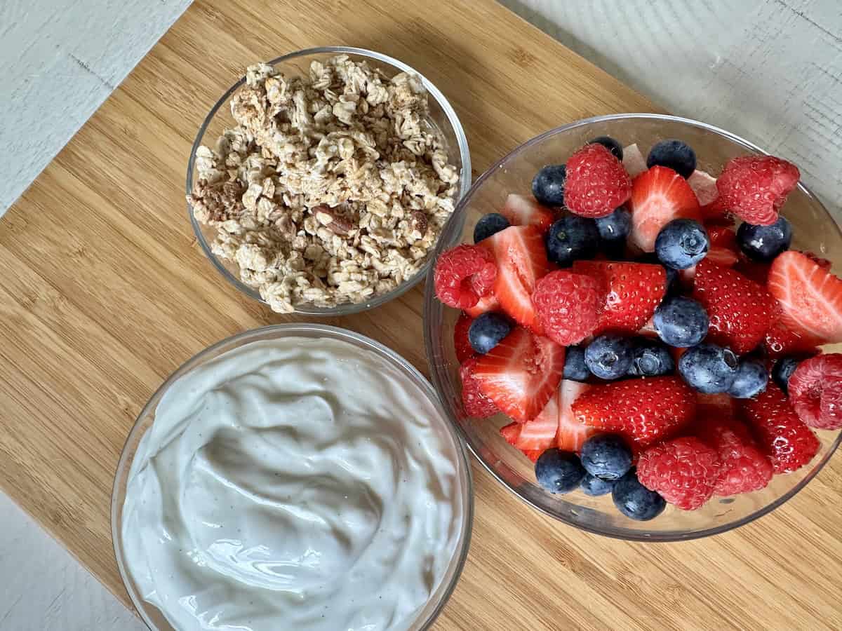 yogurt mixed berries granola in glass bowls on wood cutting board
