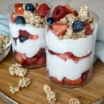 two yogurt and berry parfaits with granola on wood cutting board