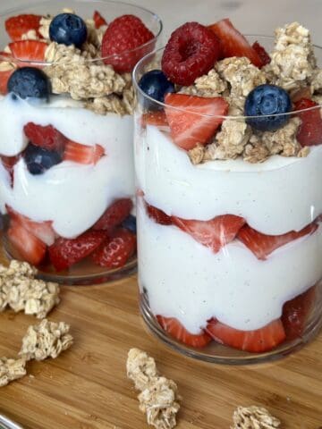 two yogurt and berry parfaits with granola on wood cutting board