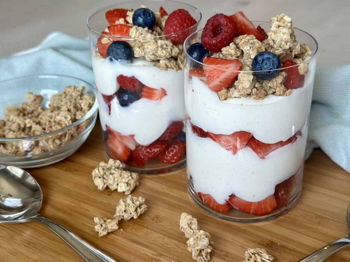 two yogurt and berry parfaits with granola on wood cutting board