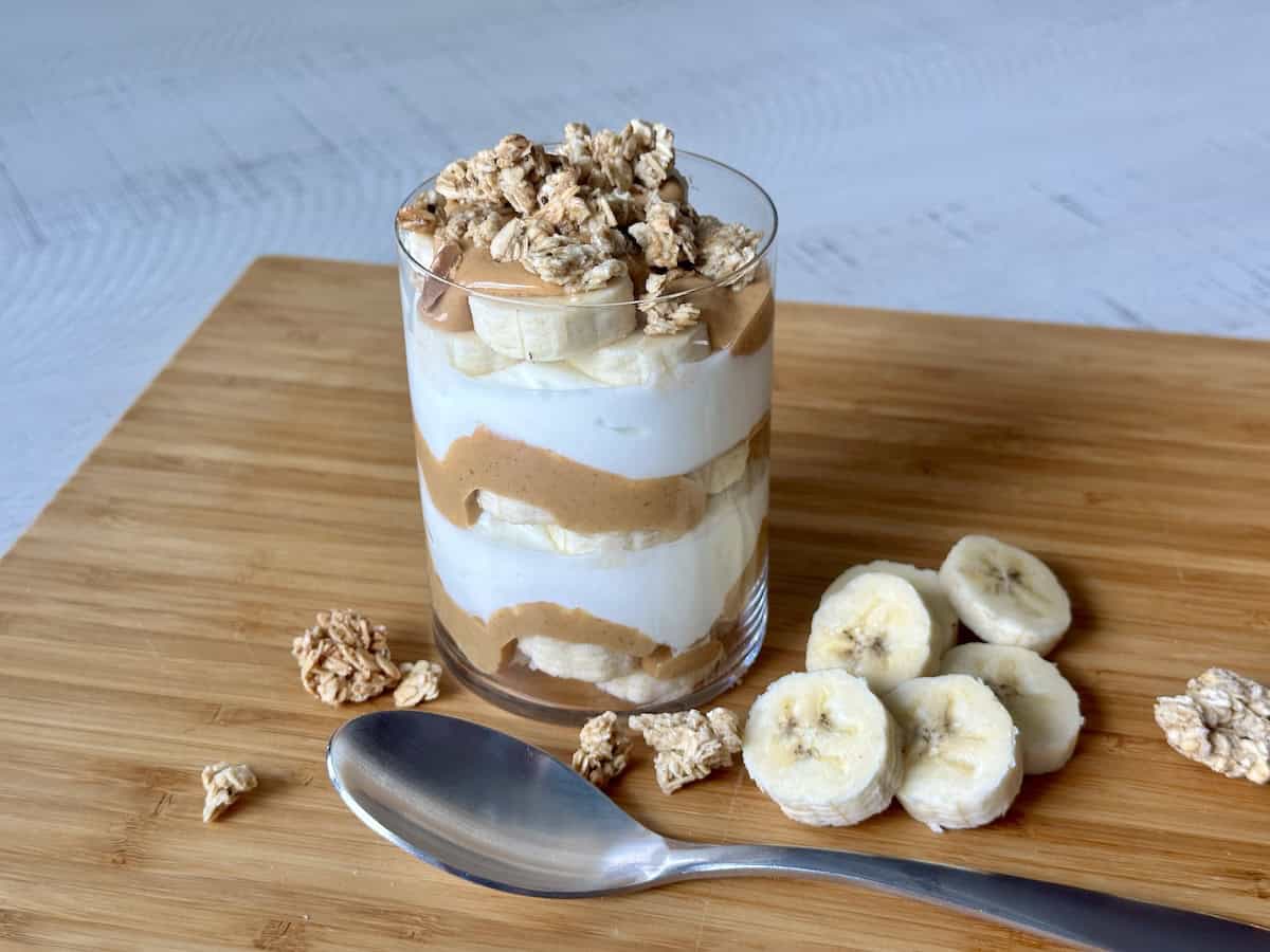 banana peanut butter and yogurt parfait on wood cutting board with granola and sliced bananas