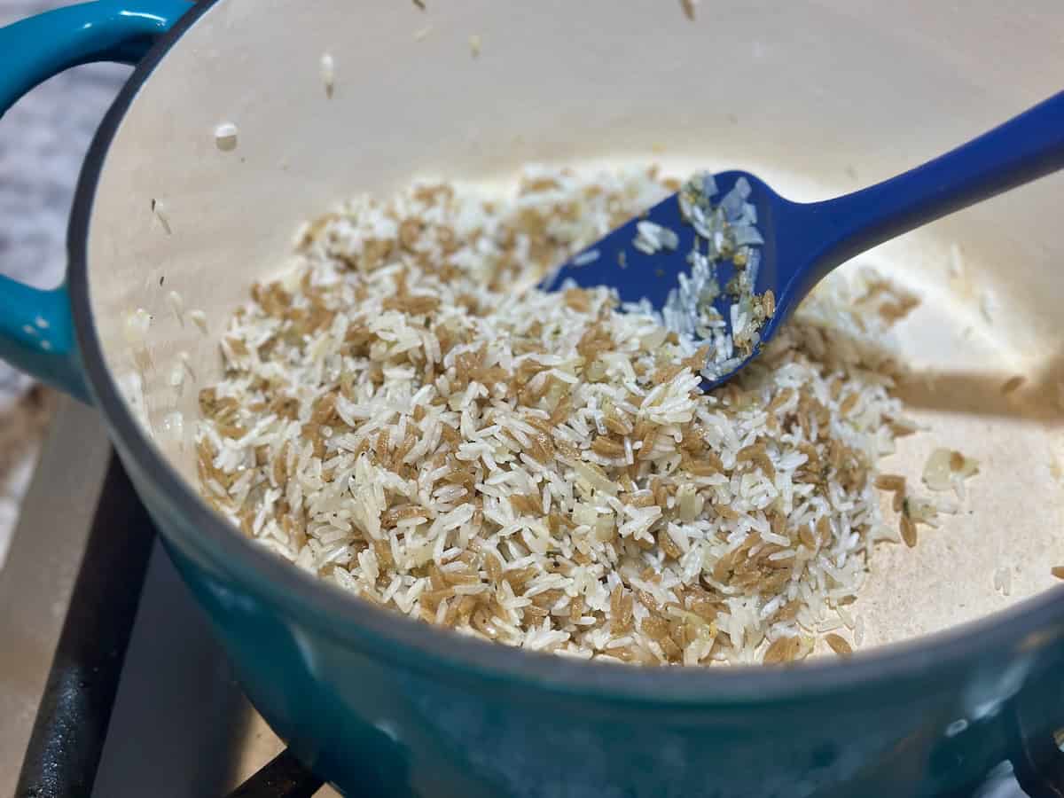 rice and orzo stirred with blue spatula in teal dutch oven