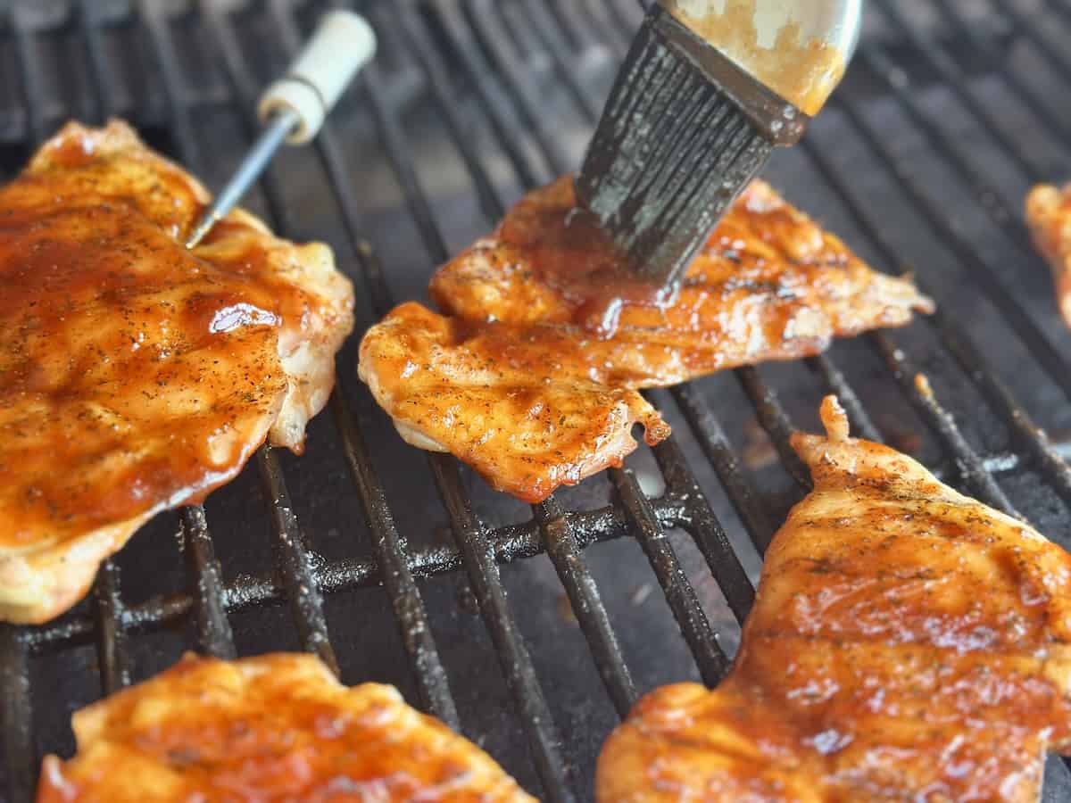 bbq chicken thighs being brushed with bbq sauce