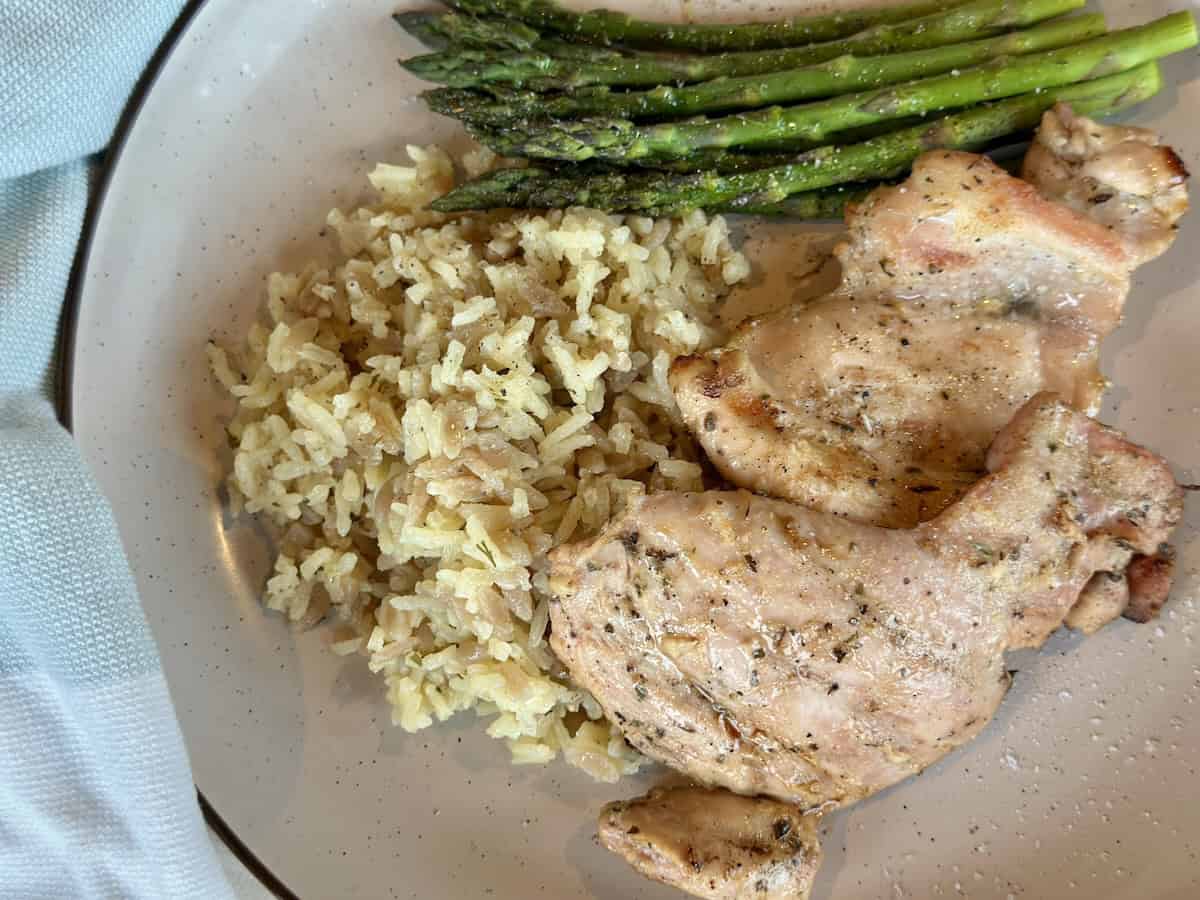 brown plate with grilled chicken thighs asparagus and rice pilaf green kitchen towel