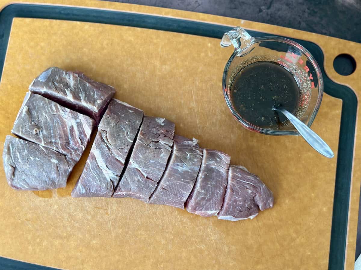 cut tri-tip roast and measuring cup of marinade on cutting board