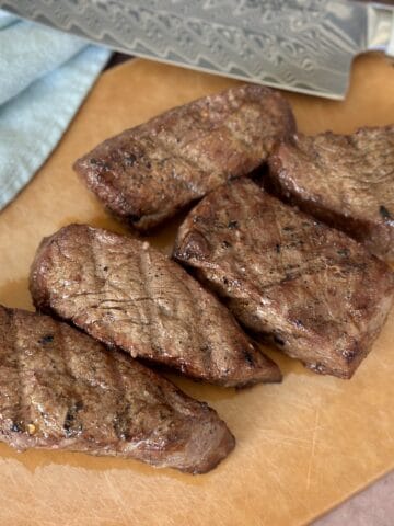 5 tri tip steaks on wood cutting board with knife